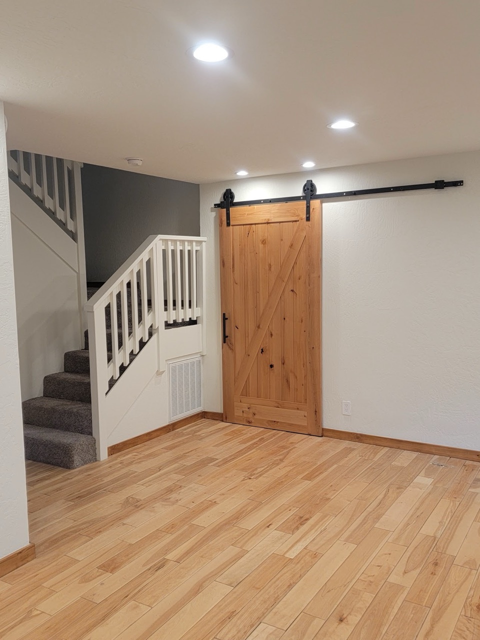 Finished room with hickory floors, a knotty alder barn door on a black rail, and a white stair rail