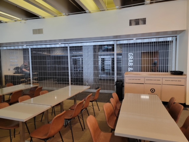 Commercial cafeteria seating with grab-and-go cases behind a security grille