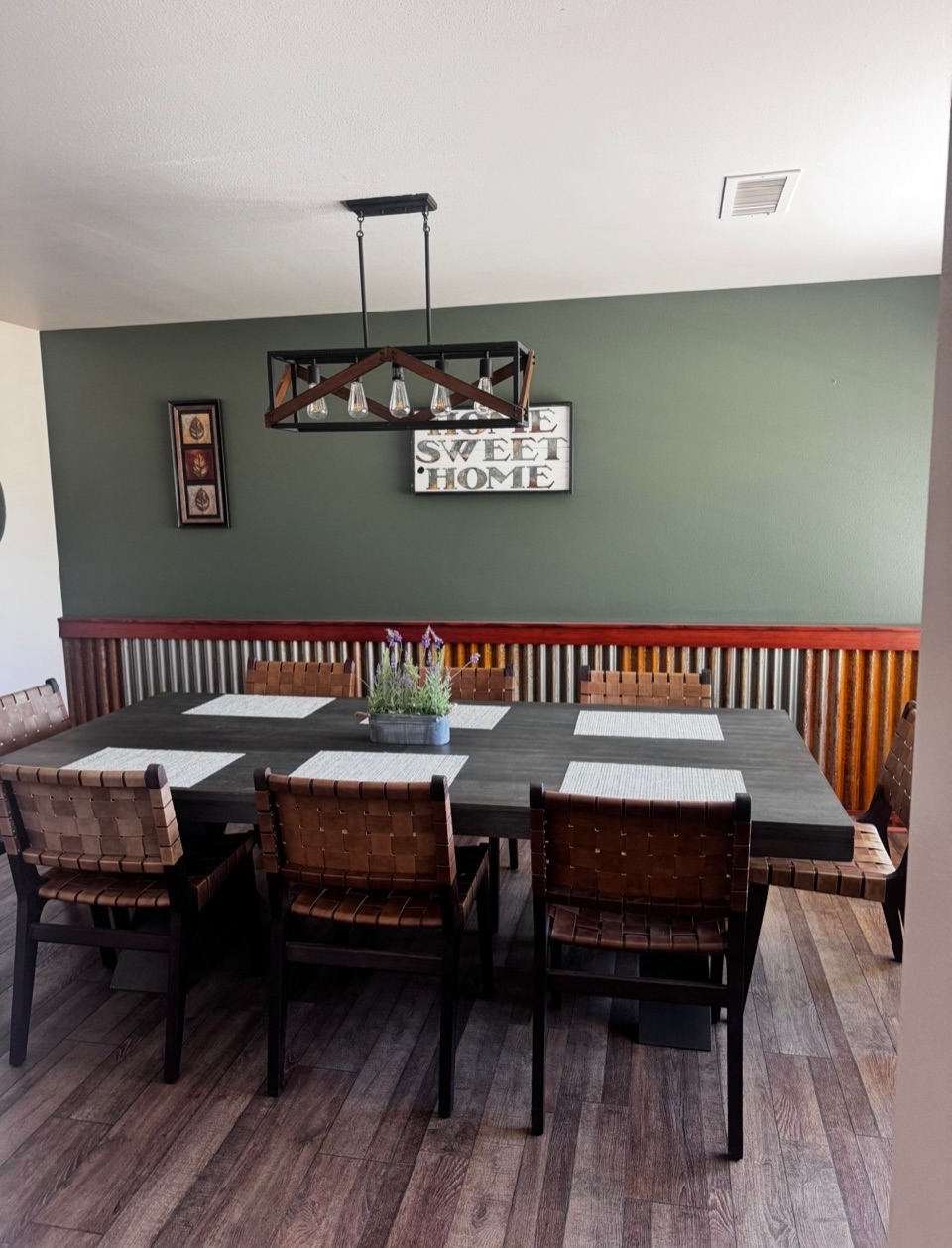 Dining room with a sage green wall, corrugated metal wainscot and a black beam chandelier