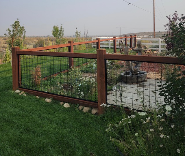 Redwood and hog-wire fence around a lawn, with a flagstone patio and water feature behind