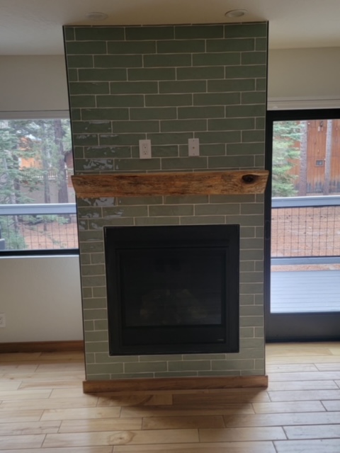 Fireplace faced in sage green subway tile with a reclaimed timber mantel and hickory floor