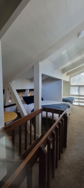 Loft bedroom tucked under a sloped ceiling behind a stained wood railing