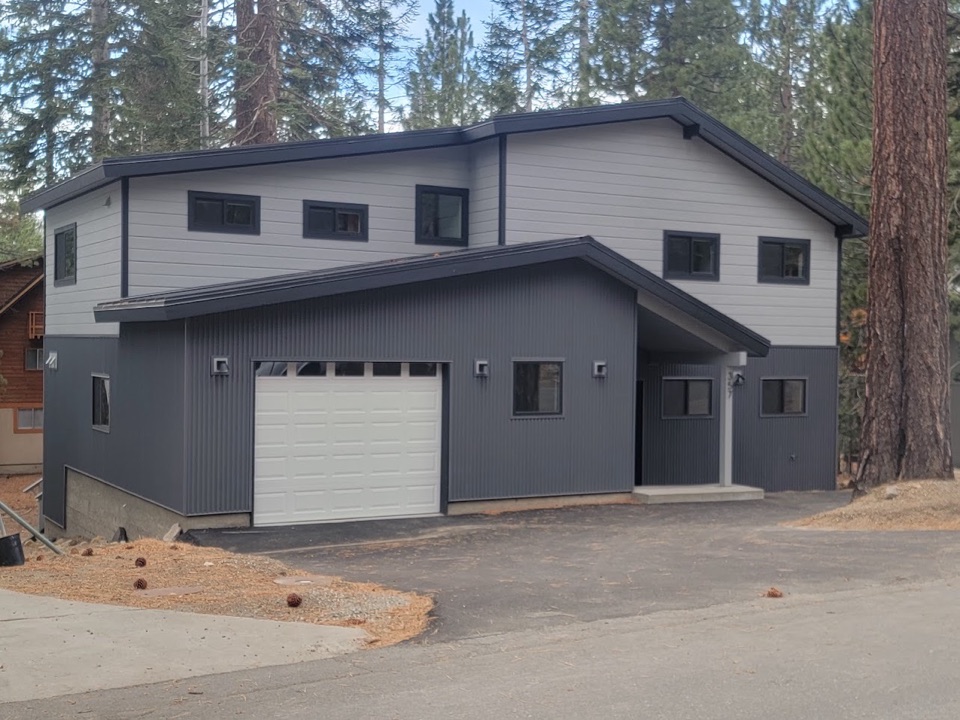 Two-storey new build in grey and white board siding under an overcast Sierra sky