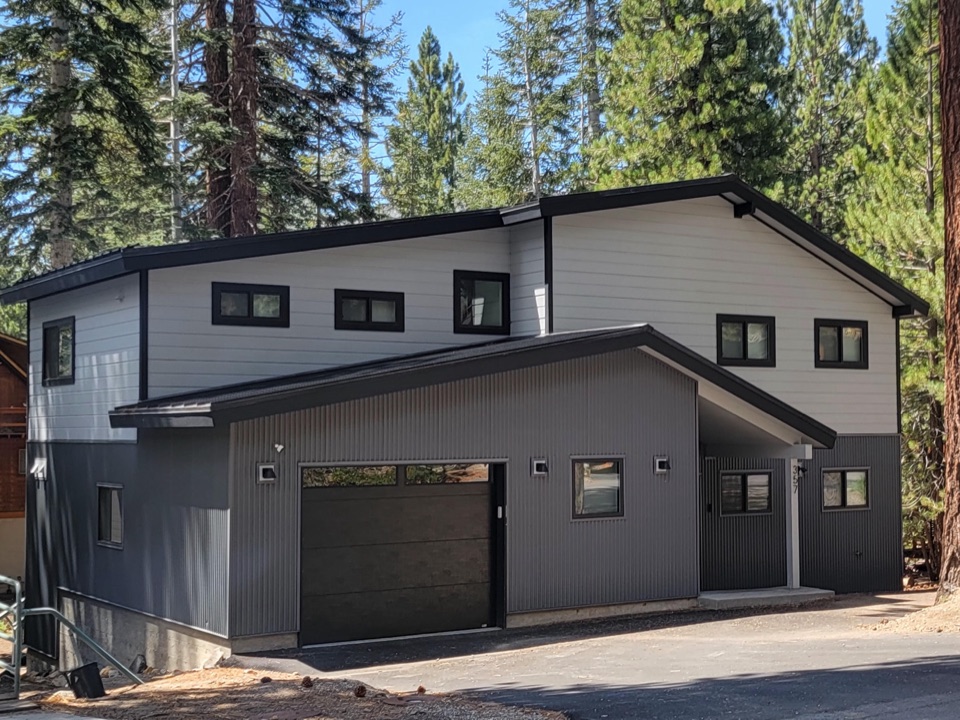 Modern mountain home with a black standing-seam roof, white lap siding and corrugated grey metal, built among tall pines