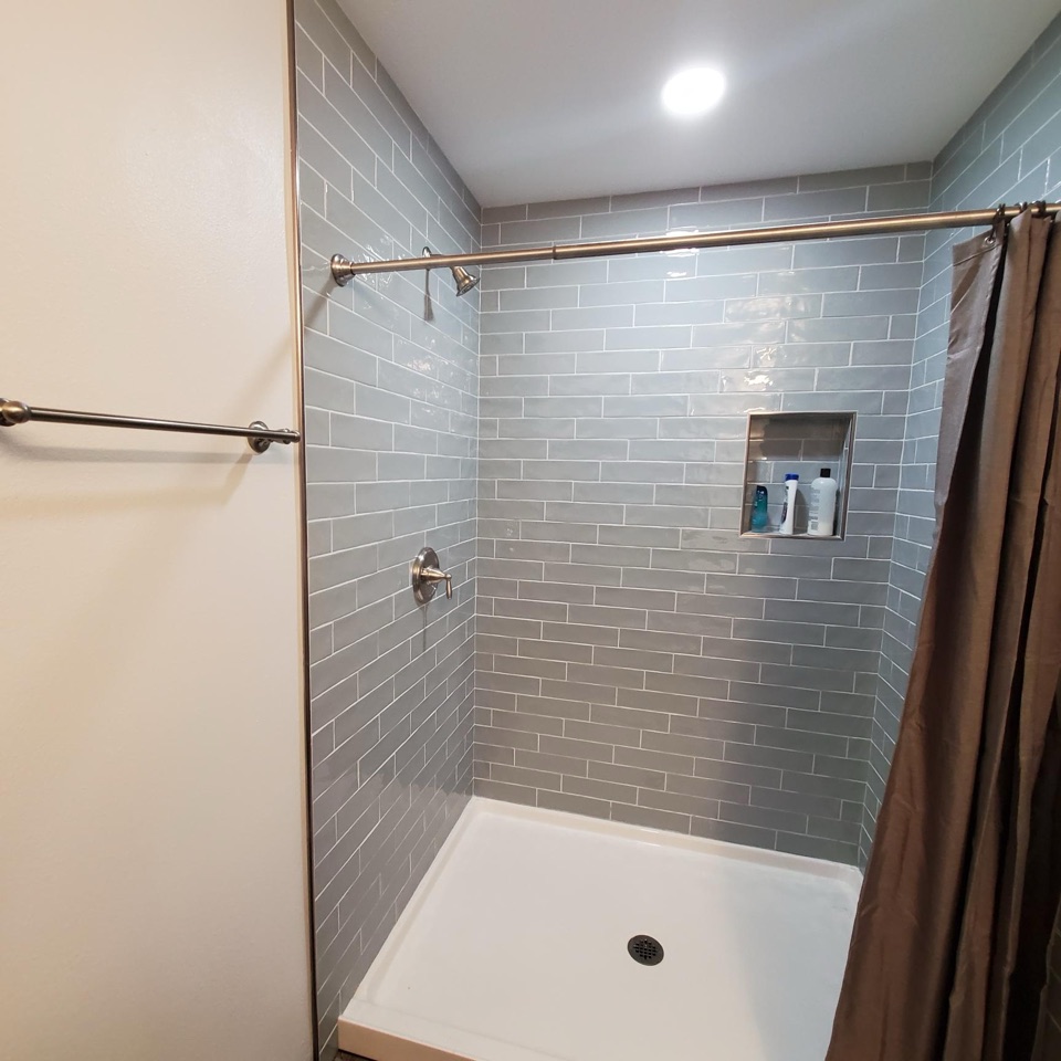 Shower lined in grey glass subway tile with a recessed niche and brushed nickel fittings