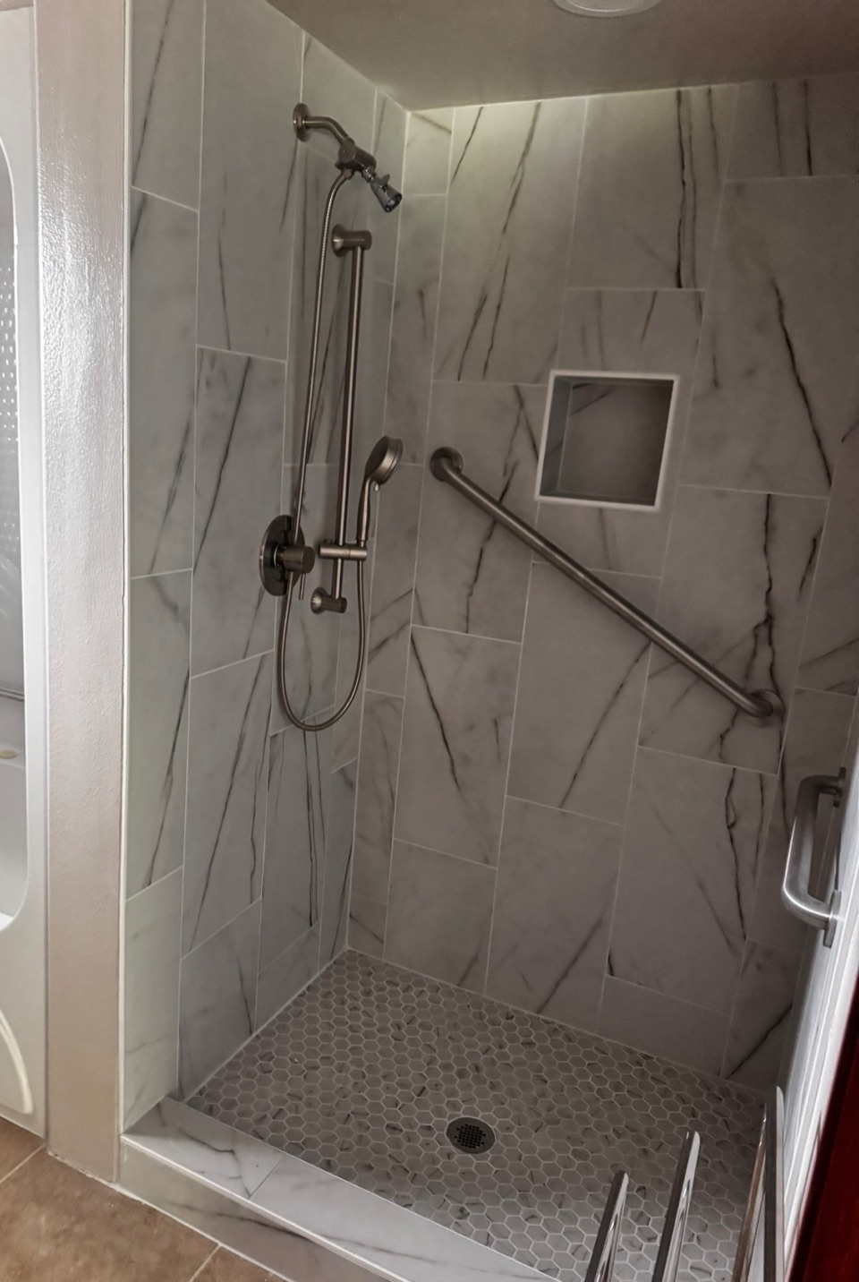 Walk-in shower tiled in marble-look porcelain with a hexagon mosaic floor, a recessed niche and a brushed nickel grab bar