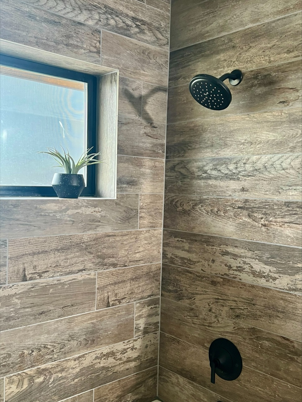 Close detail of a shower wall in wood-look plank tile with a tiled window reveal and matte black fixtures