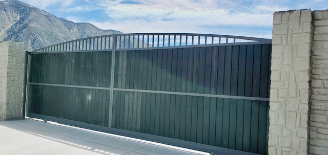 Large steel driveway gate between stone pilasters with the Sierra Nevada behind